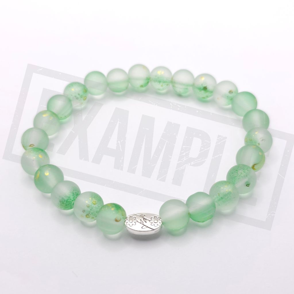 A beaded stretch bracelet made of translucent fruit green round beads with small gold flecks, featuring a central silver oval charm, displayed on a white background.