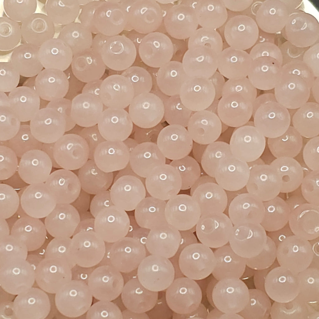 A close-up pile of small, round, pale pink translucent beads with drilled holes, filling the entire frame.
