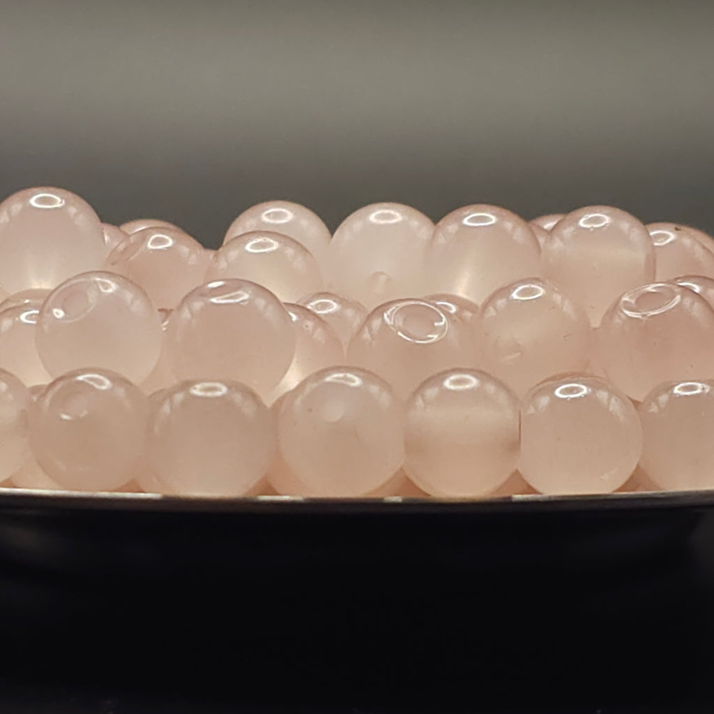 A close-up of multiple pale pink translucent oval beads arranged in rows on a dark surface against a soft gray background.