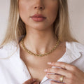 Woman wearing a gold necklace and ring, with a plain background