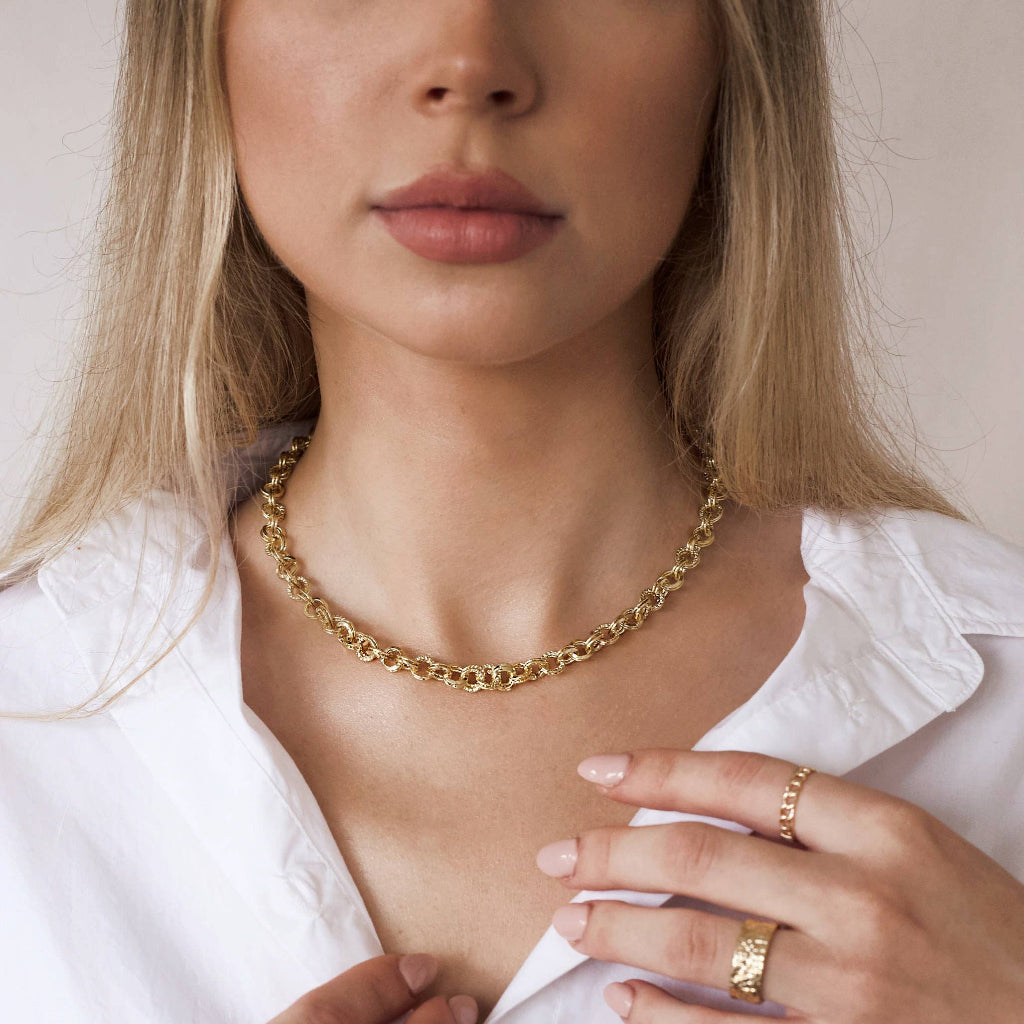 Woman wearing a gold necklace and ring, with a plain background