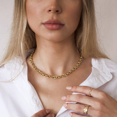 Woman wearing a gold necklace and ring, with a plain background