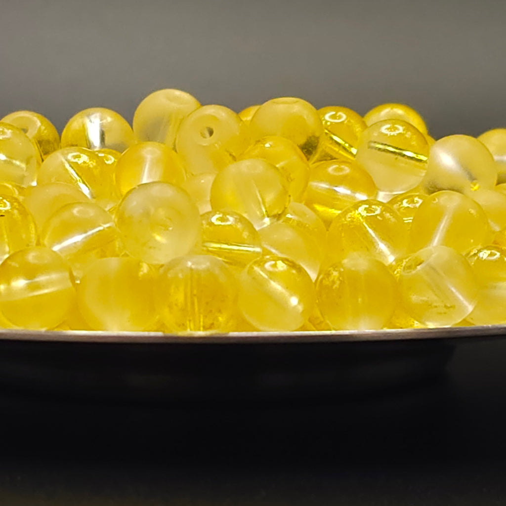 A pile of translucent yellow glass beads with a central hole, resting on a dark surface against a dark gray background.