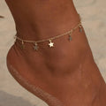 Gold anklet with star charms on a person's ankle against a blurred beach background