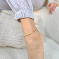 Gold anklet on a person's ankle with a blurred background