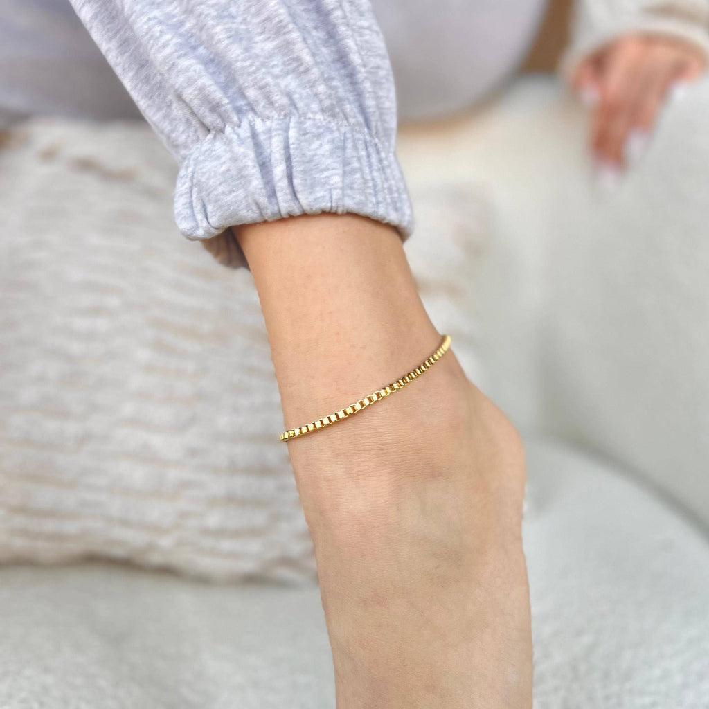 Gold anklet on a person's ankle with a blurred background