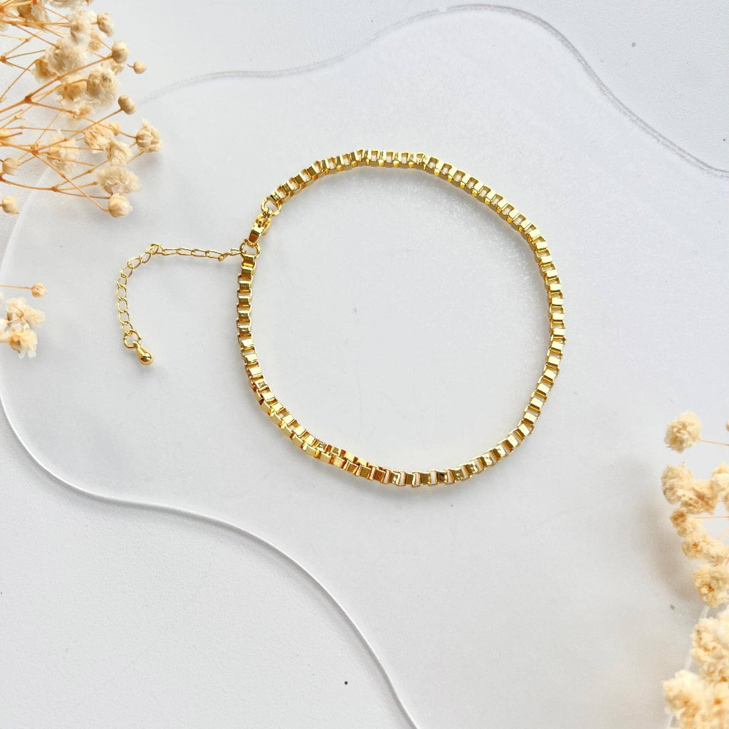 Gold bracelet on a white surface with dried flowers