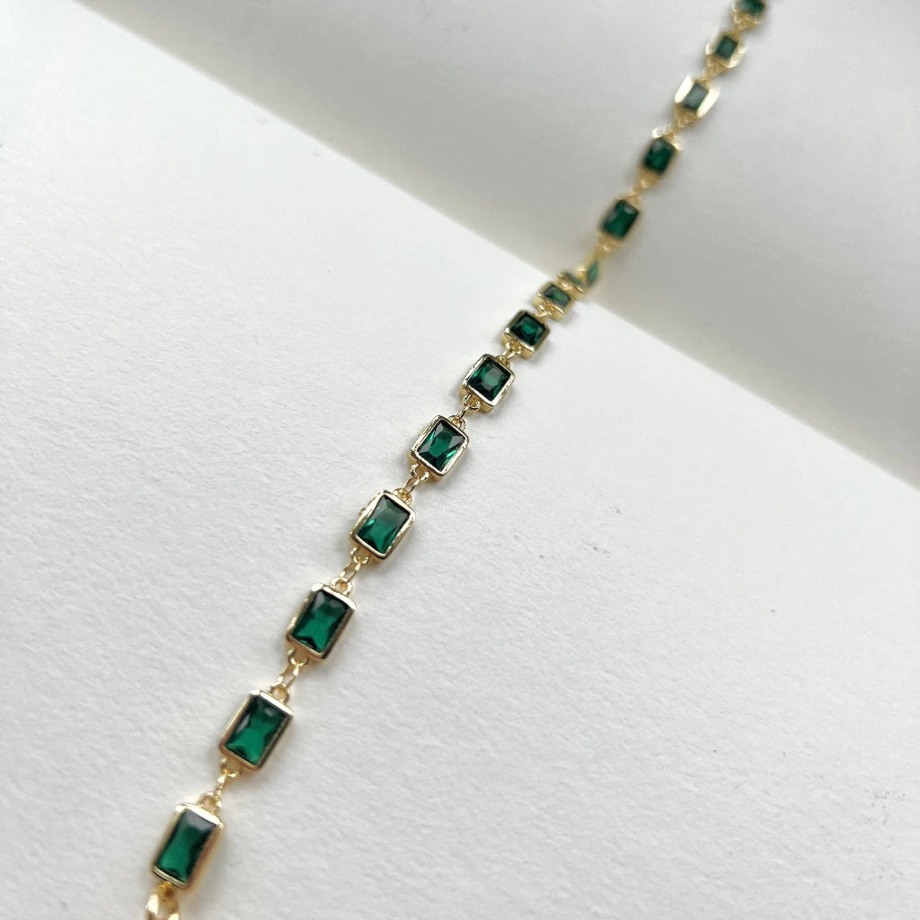 Gold bracelet with green gemstones on a white background