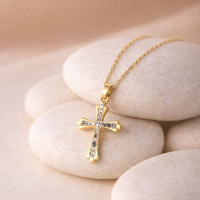 Gold cross necklace with clear stones on a beige stone surface
