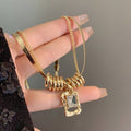 Gold necklace with a pendant held by a hand against a neutral background
