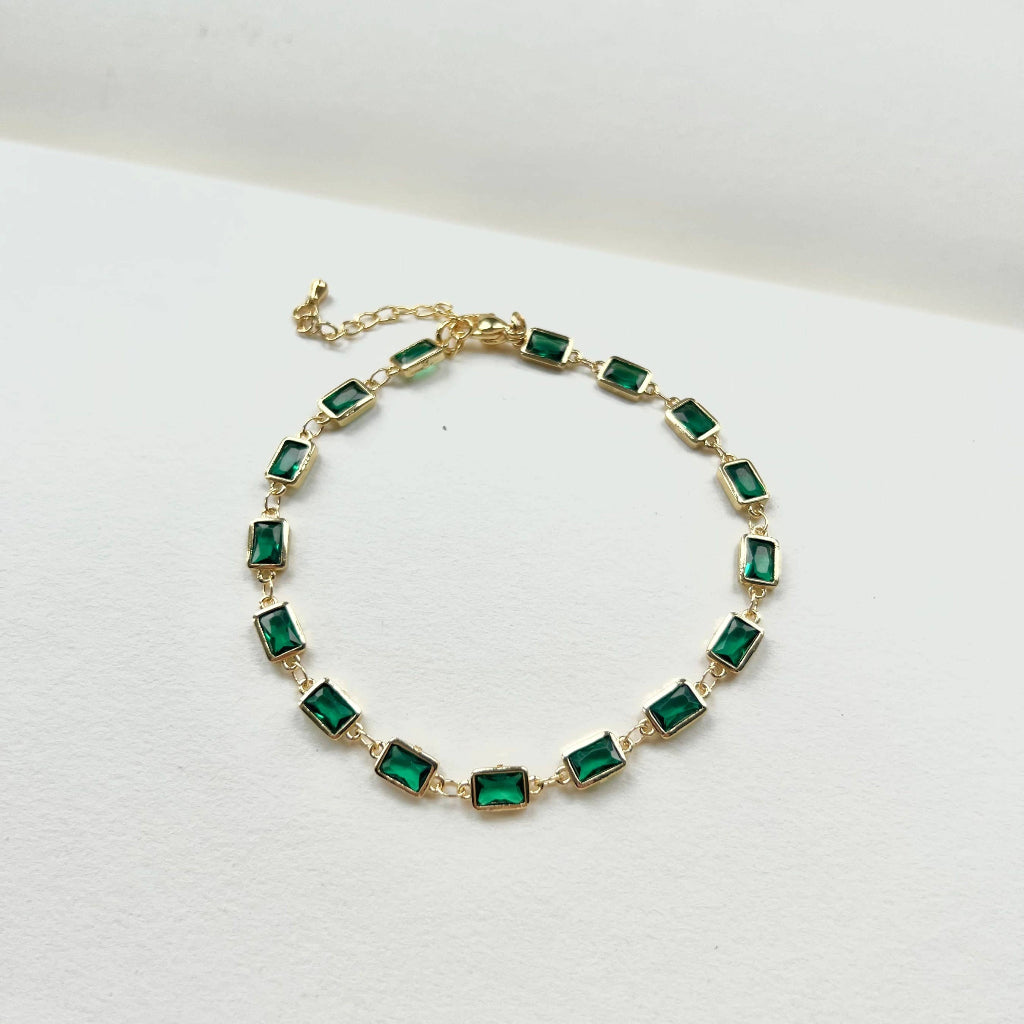 Gold bracelet with green gemstones on a white background
