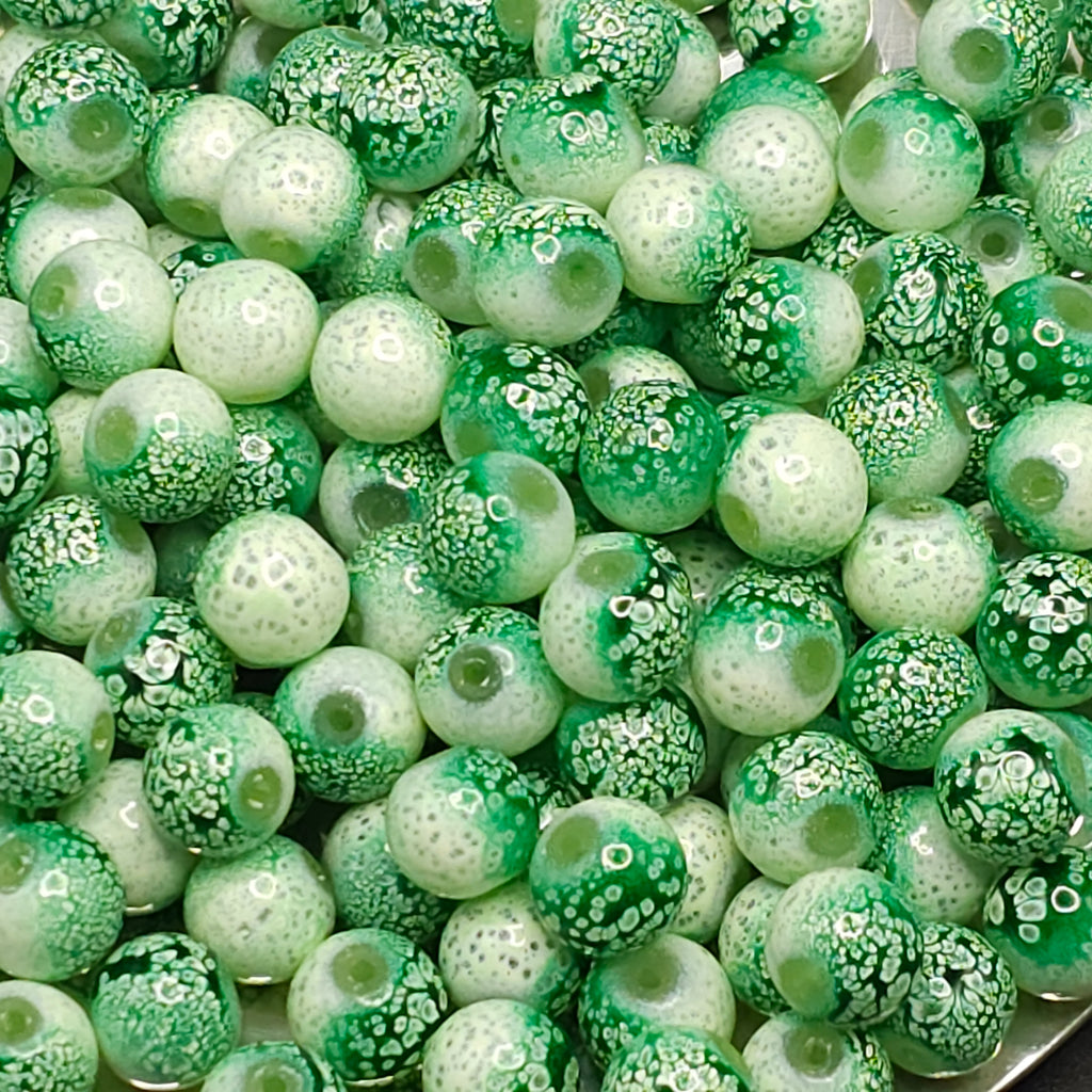 A close-up pile of round glass beads in various green and white patterns, including solid green, mottled green, and white with tiny green dots.