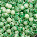 A close-up pile of round glass beads in various green and white patterns, including solid green, mottled green, and white with tiny green dots.