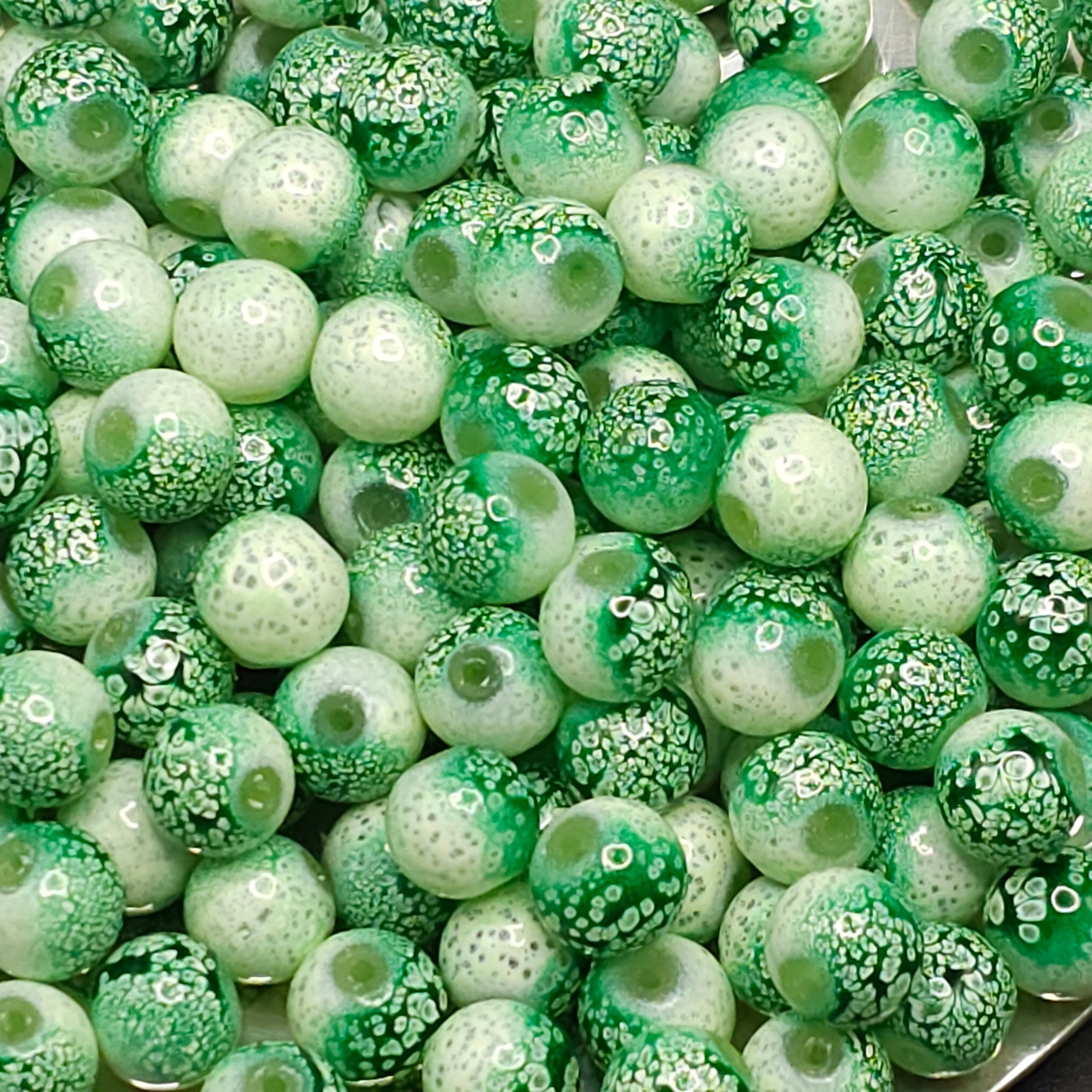 A close-up pile of round glass beads in various green and white patterns, including solid green, mottled green, and white with tiny green dots.