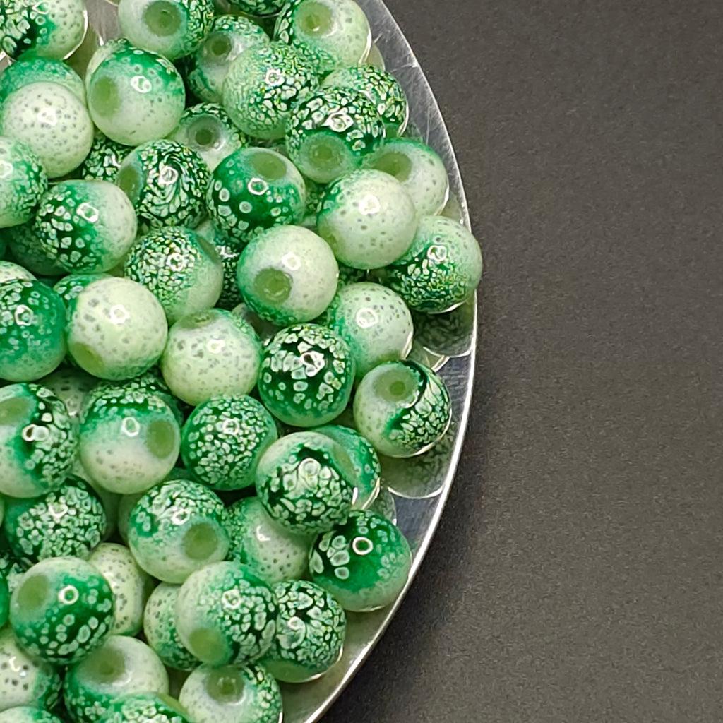 Green and white marbled glass beads piled on a silver plate against a dark gray background.