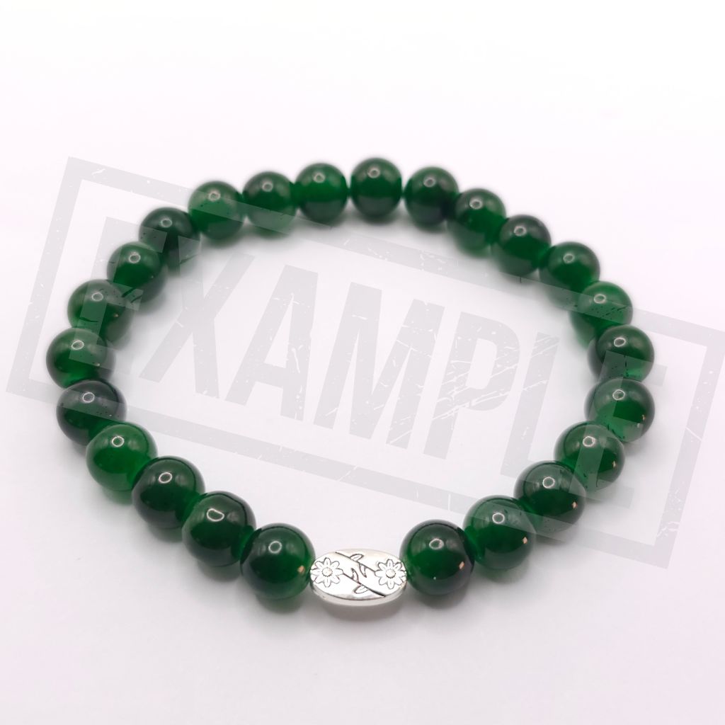 A beaded stretch bracelet made of glossy green round beads with a small silver oval charm featuring a floral design, displayed on a white background.