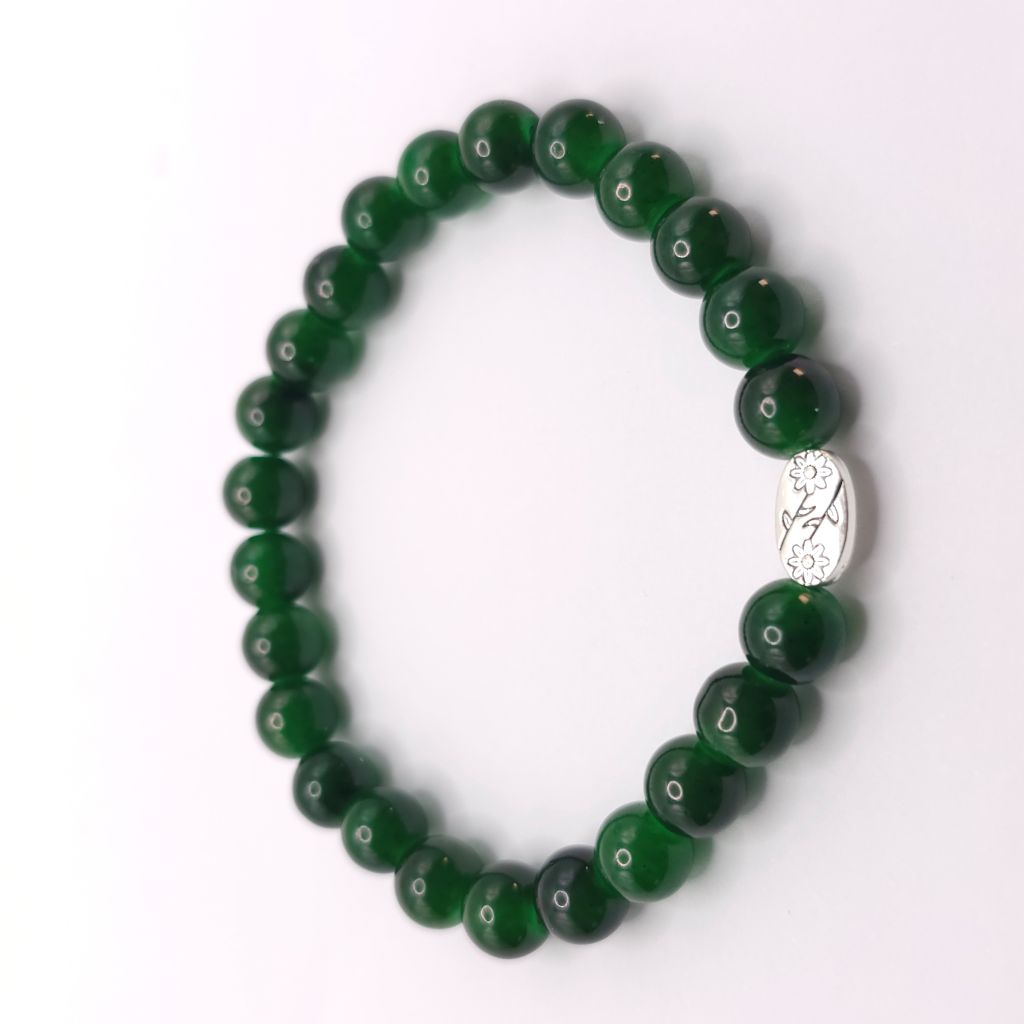 A beaded stretch bracelet made of glossy dark green round beads, featuring a small oval silver-toned charm with a floral engraving, displayed on a clean white background.