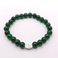 A beaded stretch bracelet made of glossy dark green round beads, featuring a small oval silver-toned charm with a floral engraving, displayed on a clean white background.