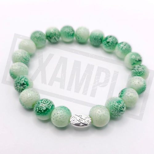 A beaded stretch bracelet made of green and white marbled glass beads, featuring a small silver-toned oval charm in the center, displayed on a white background.