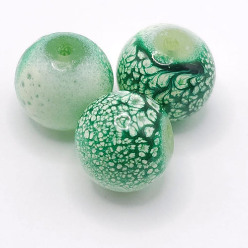 Three round glass beads in shades of green and white, featuring textured patterns and a glossy finish, arranged on a plain white background.