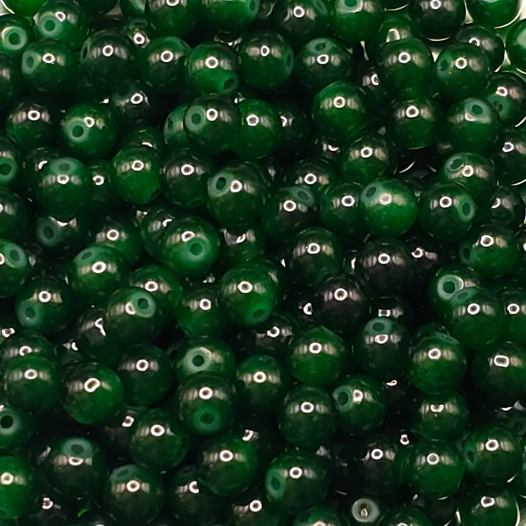 A close-up pile of glossy dark green seed beads with a single hole, filling the entire frame.