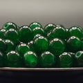 A pile of translucent green glass beads with hollow centers, resting in a dark container against a neutral gray background.
