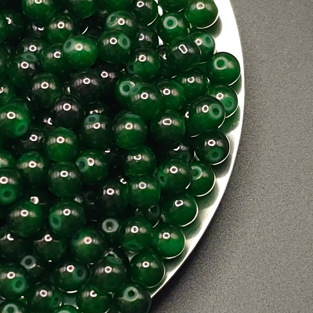 A pile of glossy, dark green round beads with central holes, arranged on a white plate against a dark gray background.