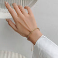 Hand wearing a gold bracelet on a neutral background