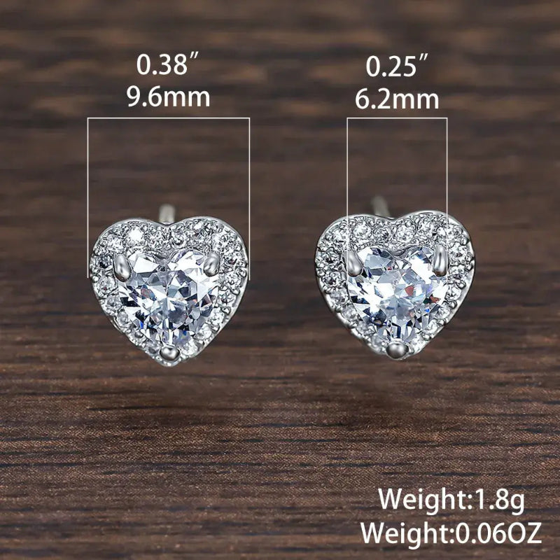 Heart-shaped earrings with measurements and weight details on a wooden surface