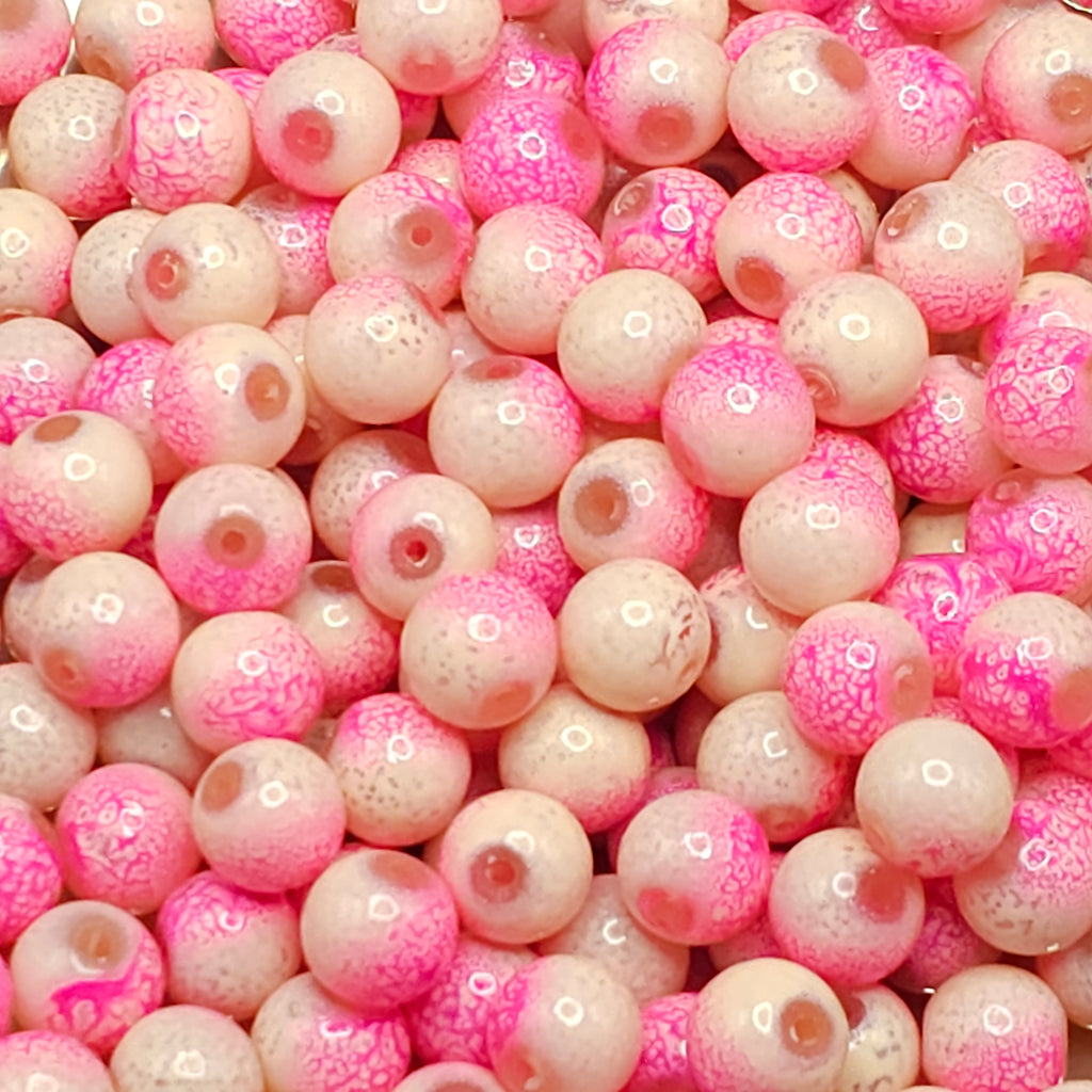A close-up pile of round glass beads in a pink and cream colorway, featuring a mottled pattern with some beads showing a warm brown center.