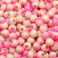 A close-up pile of round glass beads in a pink and cream colorway, featuring a mottled pattern with some beads showing a warm brown center.