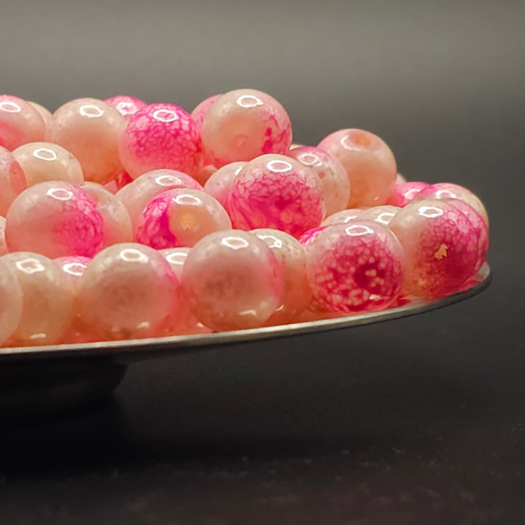 Pink and white marbled glass beads on a silver tray against a dark background.