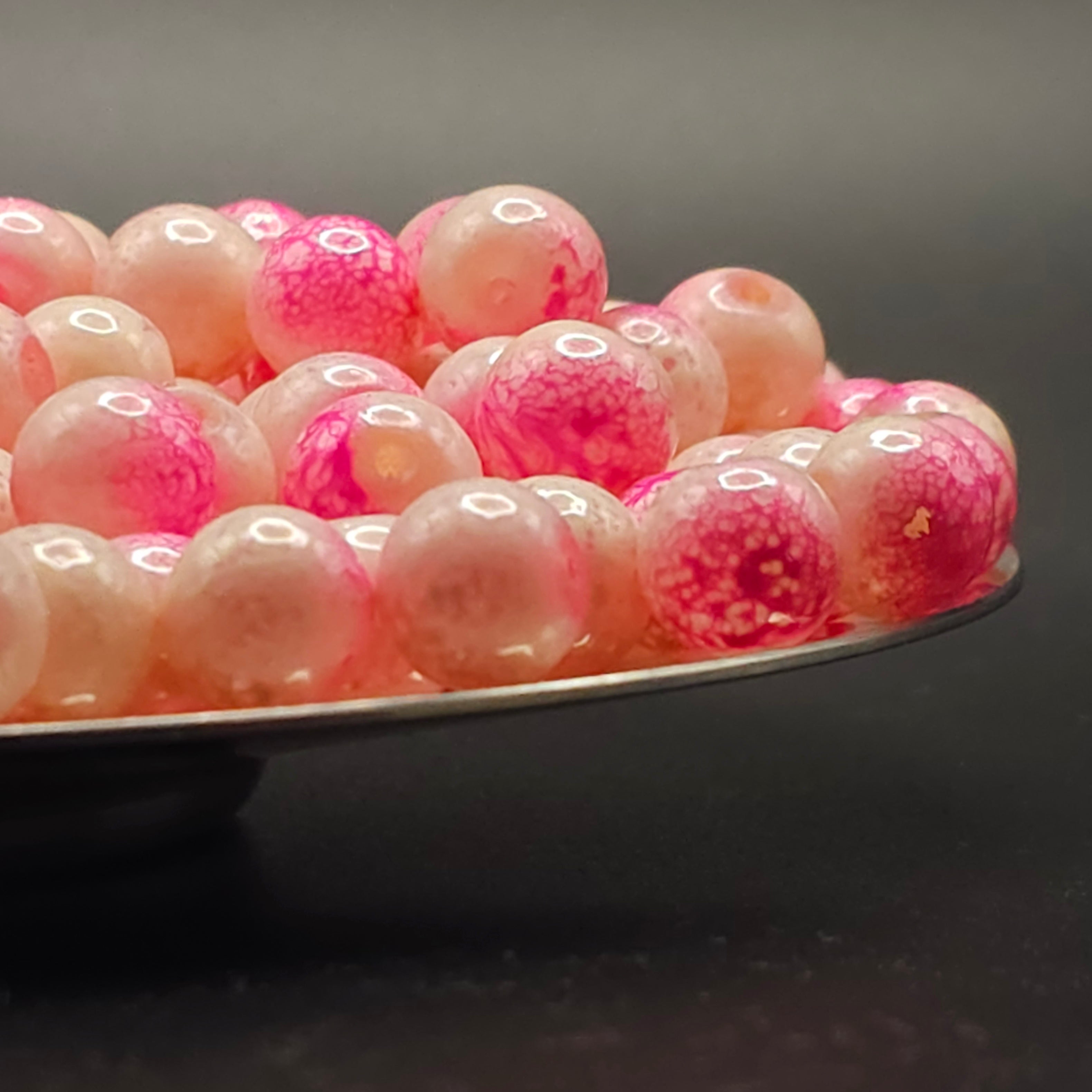 Pink and white marbled glass beads on a silver tray against a dark background.