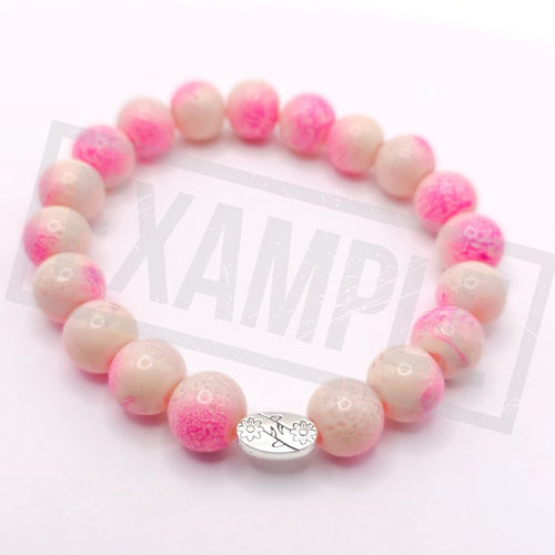 A beaded stretch bracelet made of round pink and cream marbled beads, featuring a small silver oval charm engraved with a floral pattern and displayed on a white background.