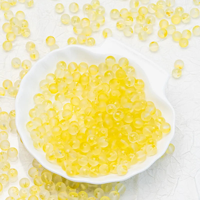 Yellow translucent silicone beads filled with liquid, presented in a white dish with more beads scattered around on a textured white background.