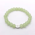 A light green beaded stretch bracelet with a small silver oval charm featuring a floral engraving, displayed on a clean white background.