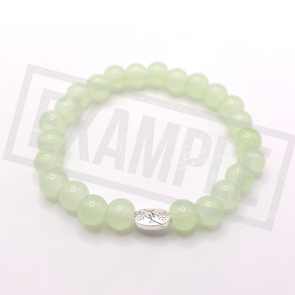 A beaded stretch bracelet made of light green glass beads with a silver-toned oval charm featuring a floral design, displayed on a white background.