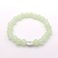 A beaded stretch bracelet made of light green translucent round beads with a small silver-toned oval charm featuring a floral design, shown on a plain white background.