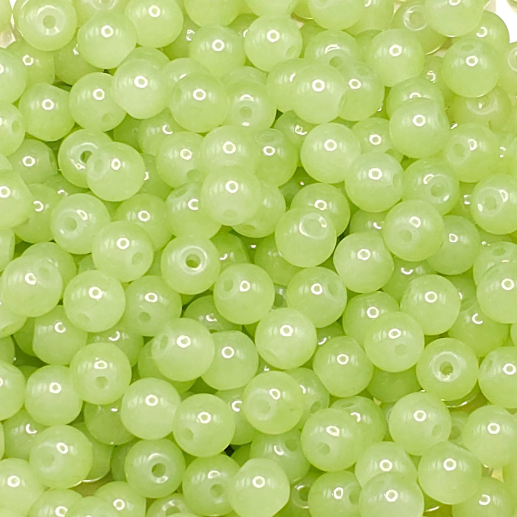 A close-up pile of small, round, light green seed beads with a glossy finish and a central hole.