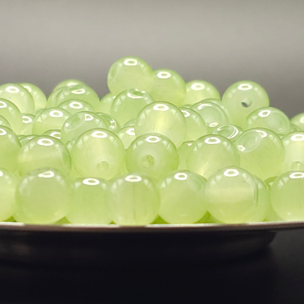 A pile of round, translucent pale green beads with holes, displayed on a dark surface against a neutral gray background.