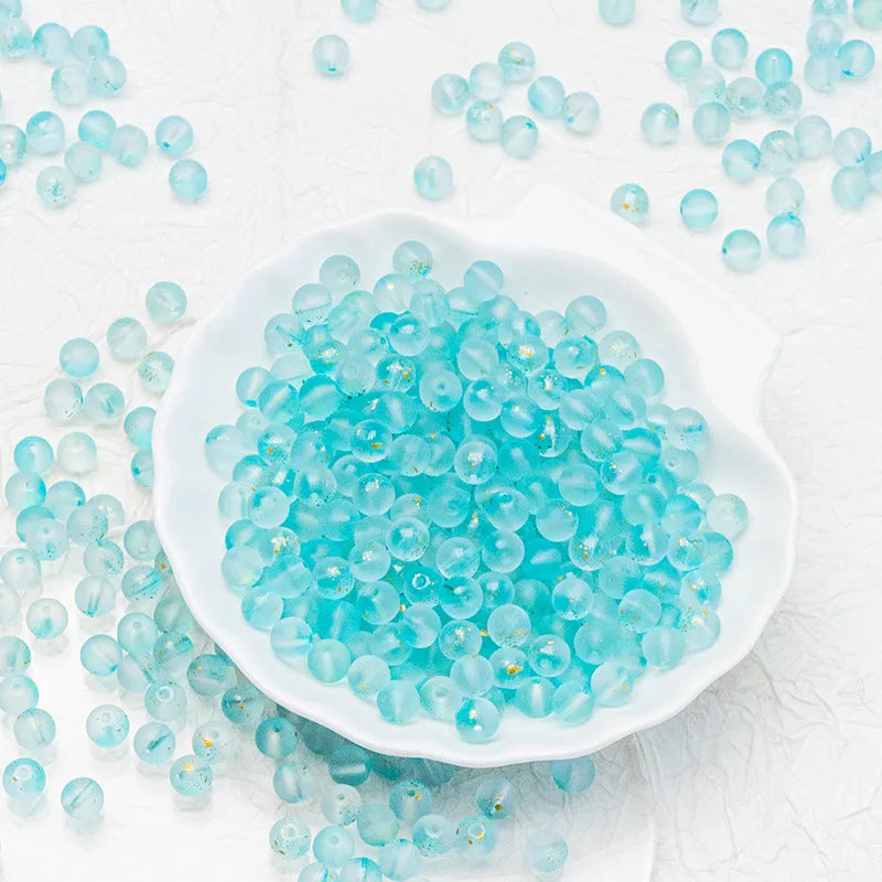 Light blue translucent round beads scattered around and piled in a white scalloped dish on a white textured background.