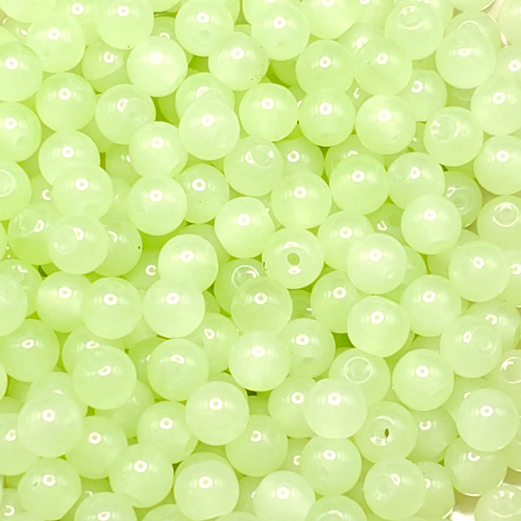 A close-up pile of small, round, translucent pale yellow-green beads with a glossy finish.