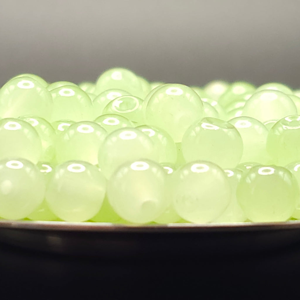 A close-up of many small translucent pale green beads or boba pearls piled in a shallow dish against a dark background.