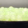 A close-up of many small translucent pale green beads or boba pearls piled in a shallow dish against a dark background.