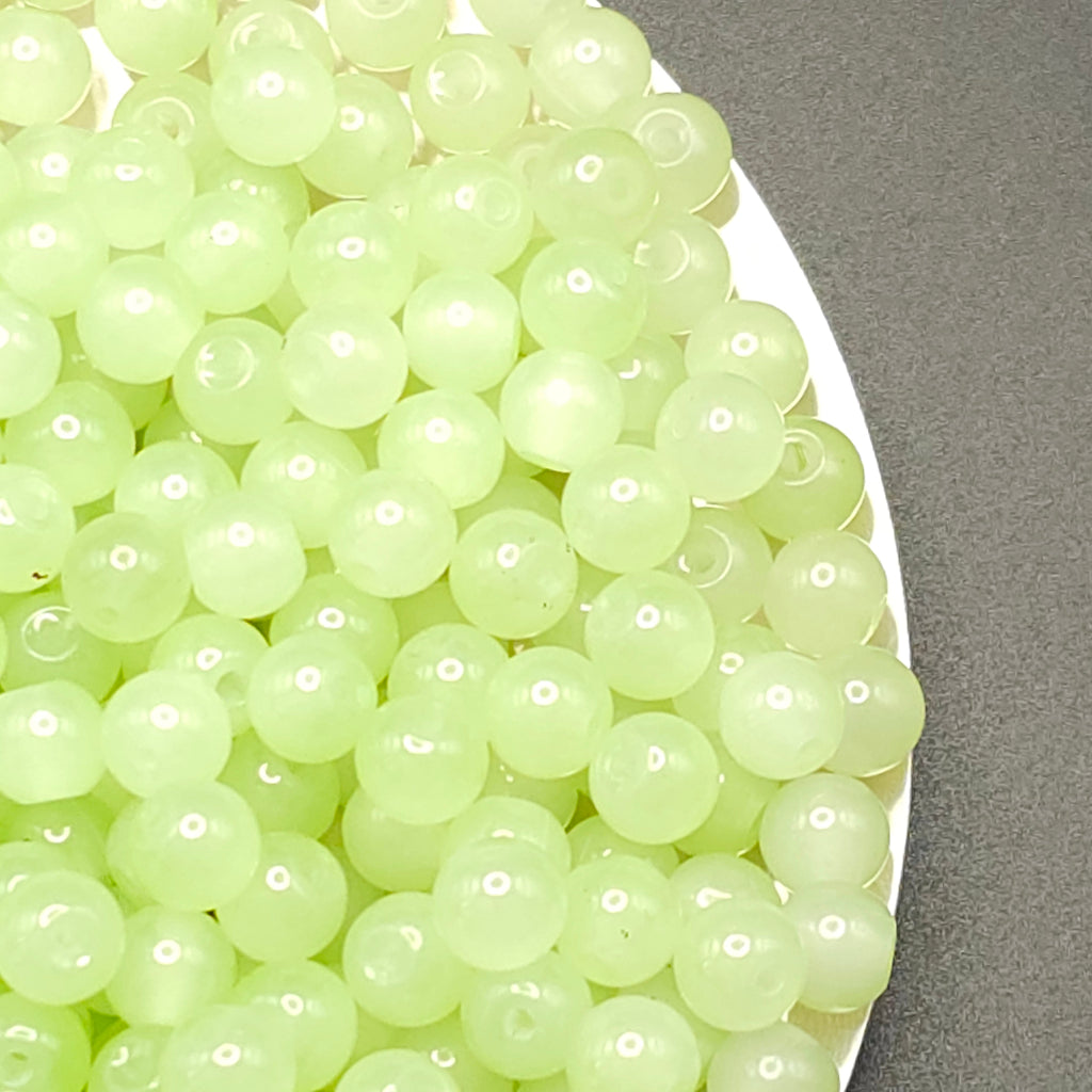 A close-up of many small translucent pale green beads or boba pearls piled on a white plate against a dark gray surface.