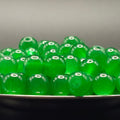 A pile of translucent green glass beads with hollow centers, resting on a dark surface against a neutral gray background.