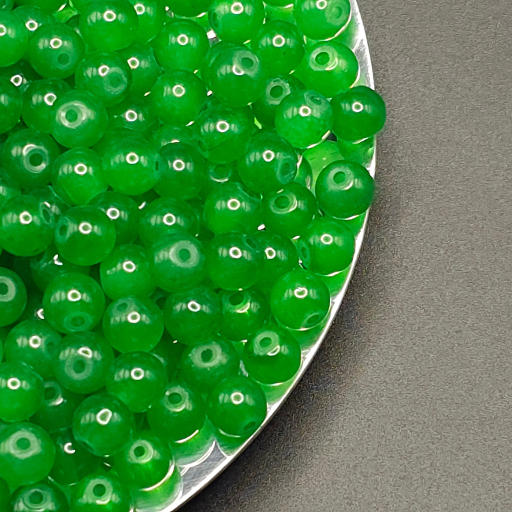 Green translucent round beads with central holes, piled on a silver scalloped dish against a dark gray background.