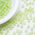 Light green translucent round beads scattered on a textured white surface, with more beads piled in a white dish in the upper left corner.