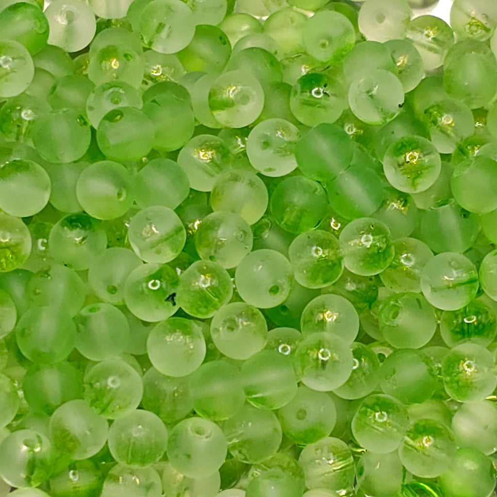 A close-up pile of small, round, translucent light green beads with a frosted finish.