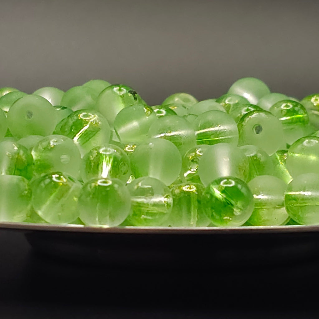 A pile of round, translucent light green glass beads with a central hole, resting on a dark surface against a dark gray background.